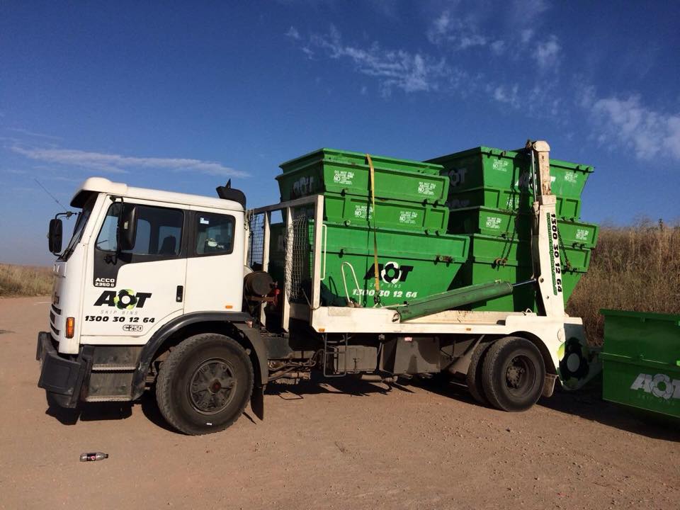 Green and white truck with skip bins loaded onto the back