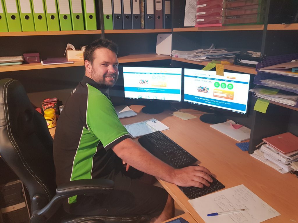 Smiling man in green shirt sits at computer desk